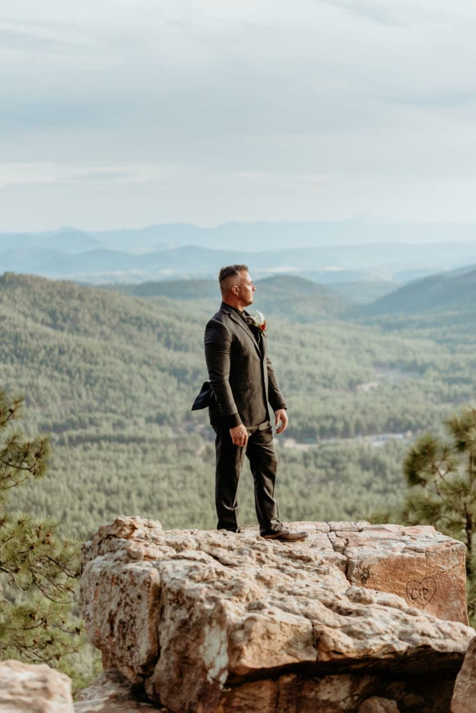 Groom standing in his black suit at the edge of the Mogollon Rim