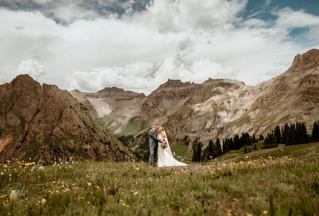 Couple embraces in front of Colorado mountains with wild flowers in front of them during their Colorado elopement