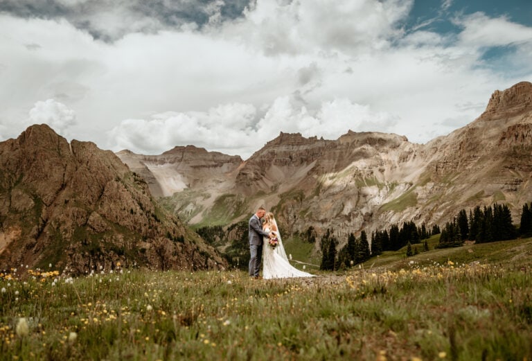 Couple embraces in front of Colorado mountains with wild flowers in front of them during their Colorado elopement