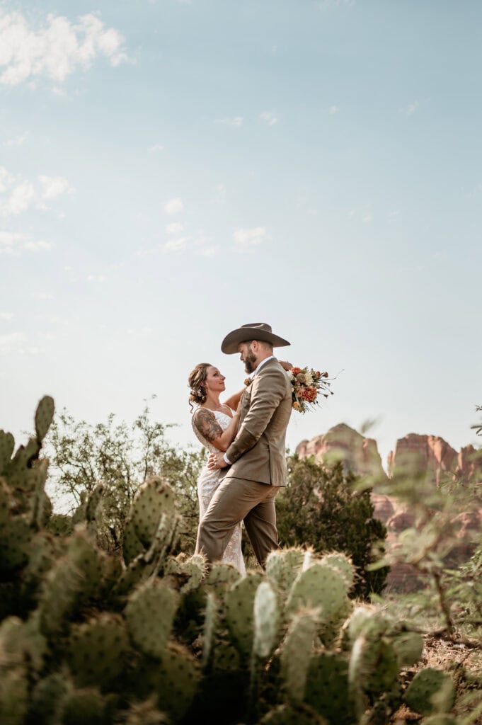 wedding couple embraces surrounded by prickly pear cactus during with Cathedral Rock in the background