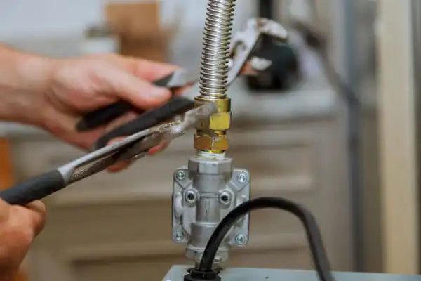 Hands using wrenches to tighten a fitting on a flexible gas line connected to a metal valve.