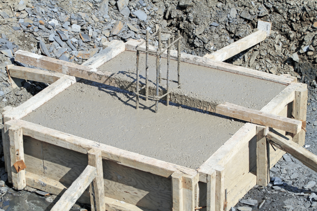 Fresh concrete foundation footing with rebar reinforcement, surrounded by wooden formwork and set in rocky soil at a construction site, highlights the precision of concrete construction and expert excavation work.