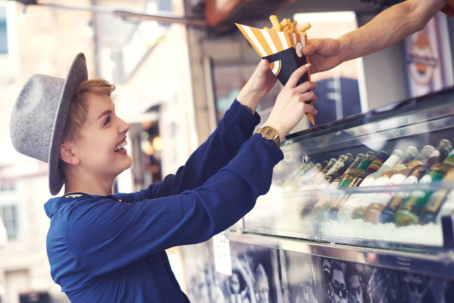 A smiling woman holds a cone of freshly made french fries ordered from a food truck.