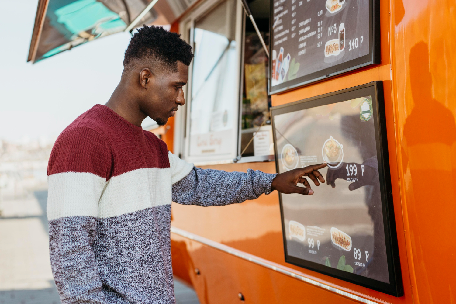 A man browses the menu hanging on the outside of a food truck.
