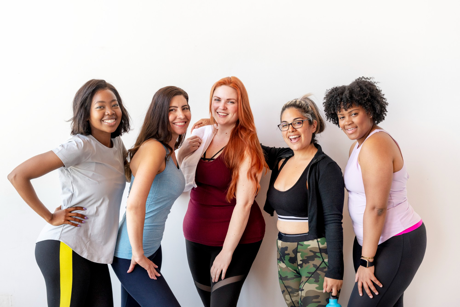 A group of five women in workout clothing, all smiling. The key to gym staff retention is happy staff in a great workplace environment.