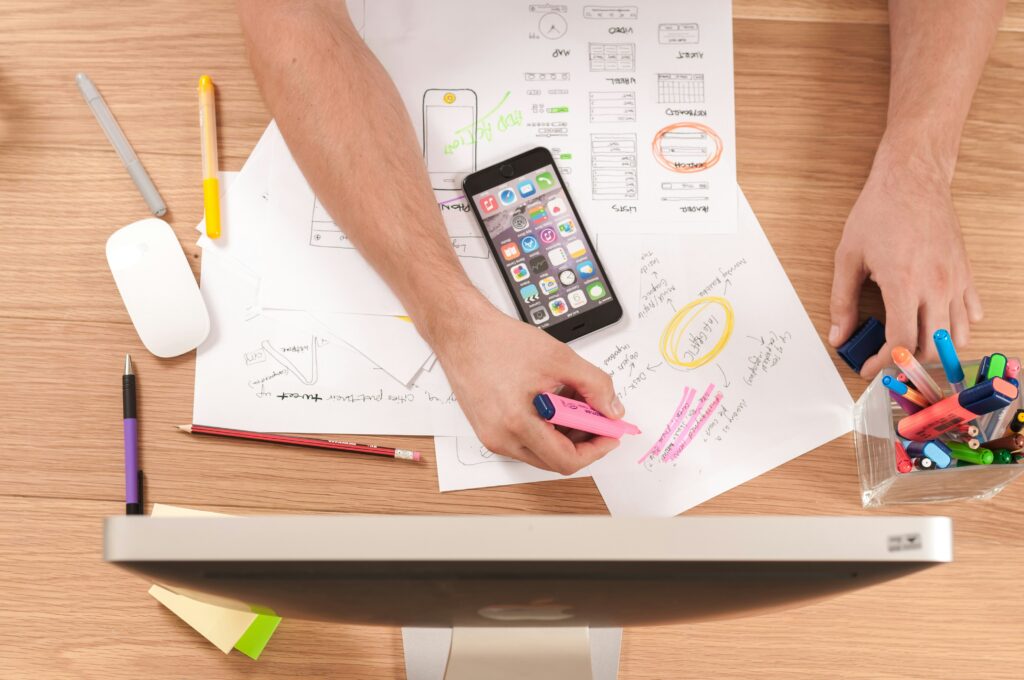 Man working at a desk with papers, pens, smart phone, and a monitor.