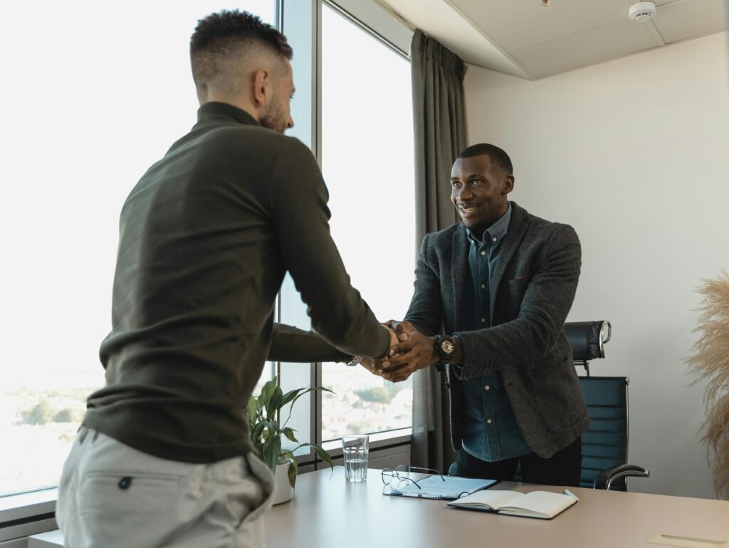 Two men shaking hands over a desk after an interview.