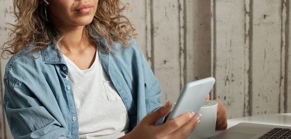 Latinx woman using her mobile phone while siting at a desk with a laptop and a mug in hand