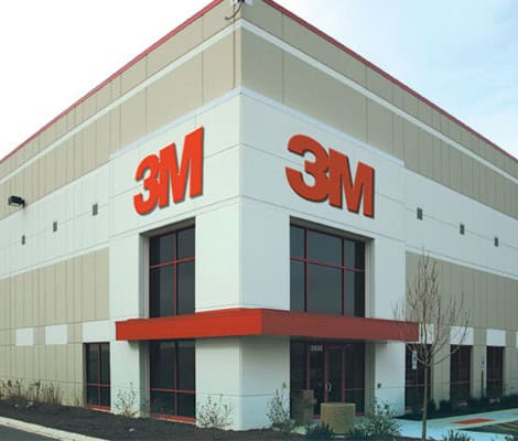 The corner of a 3M building with glass walls and entrances. A big "3M" is on each wall.