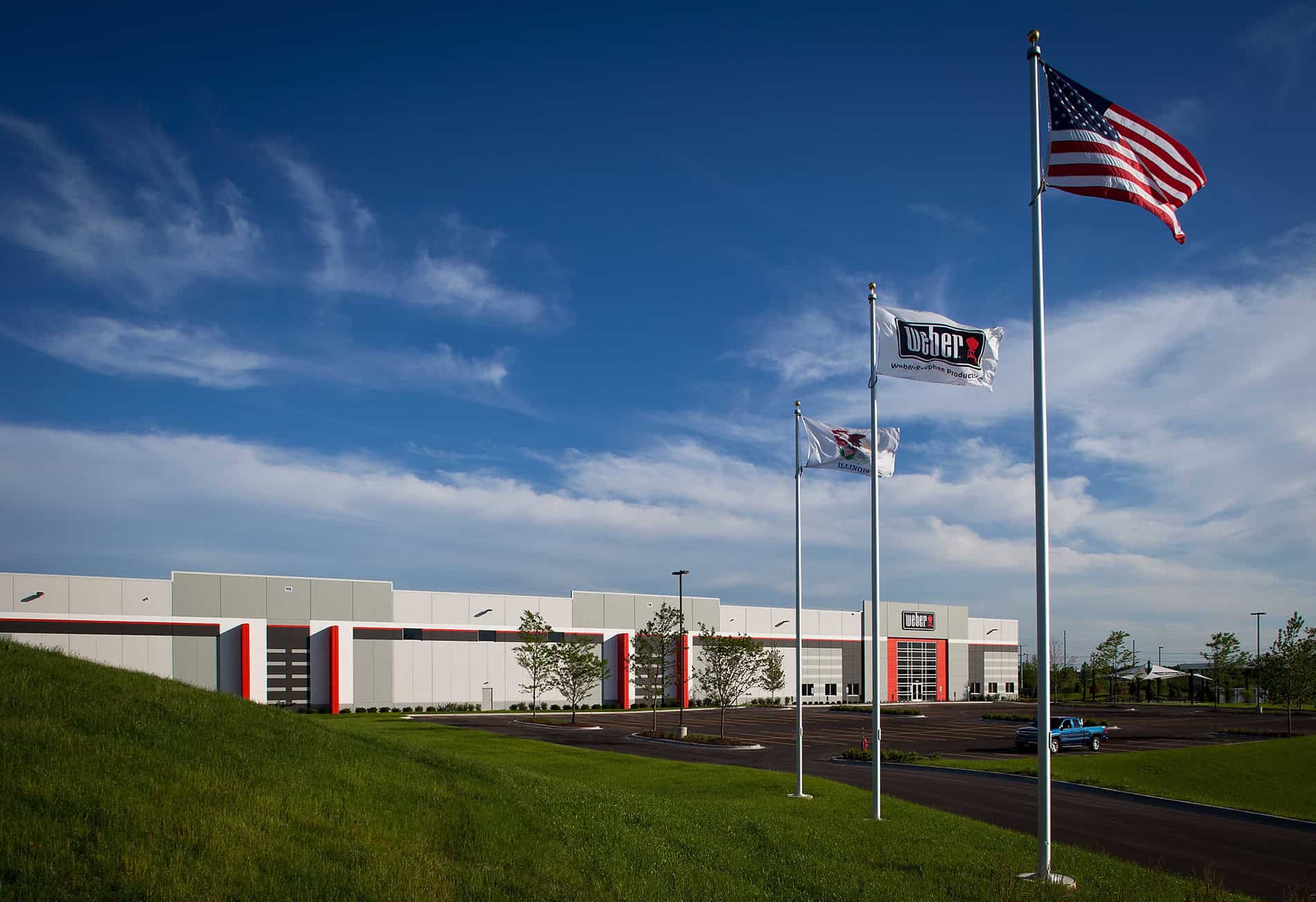 Three flagpoles line up in front of the Keeley Construction built Weber-Stephen Distribution Facility in the background.