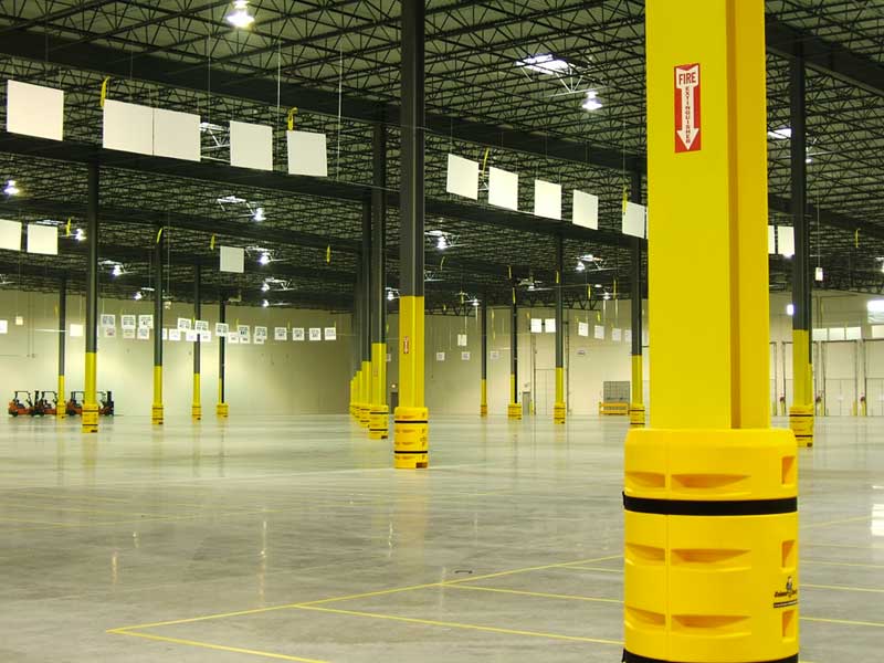 An empty warehouse has yellow pillars throughout the otherwise open room and a black metal grid ceiling. This facility is a new construction project for Toyota by Keeley Construction Inc.