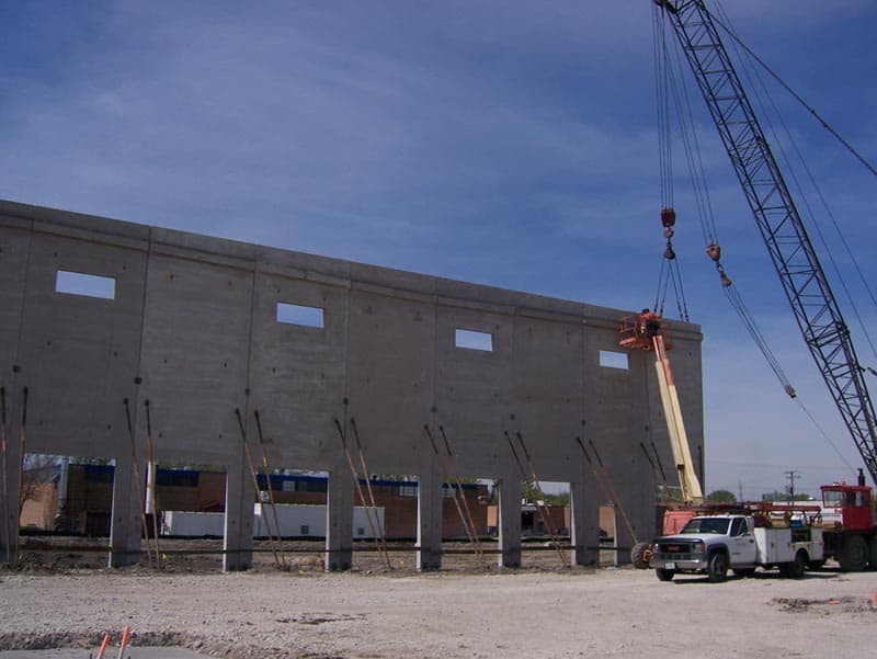 An unfinished wall supported by angled beams dominates the view. A crane and other equipment give the workers access to the top of the unfinished Toyota project built by Keeley Construction, Inc.