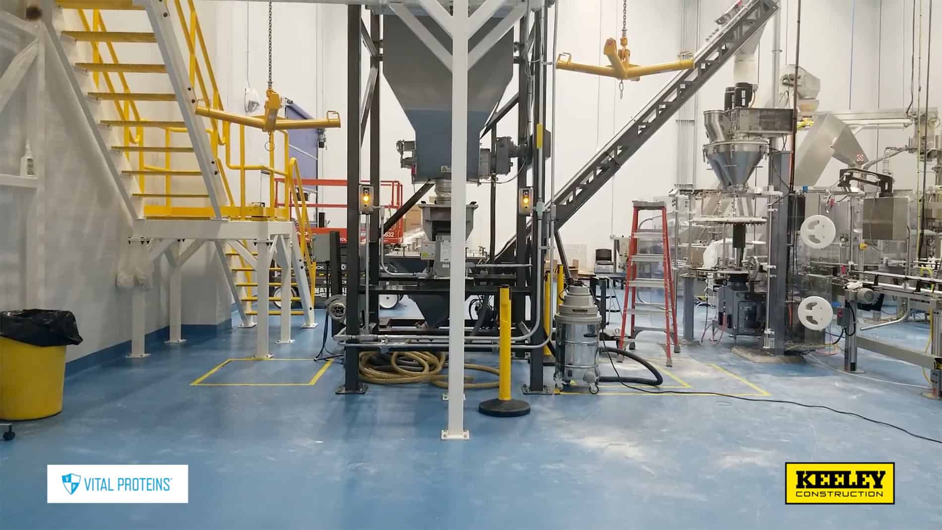 A Vital Proteins production plant interior with shiny equipment, yellow stairs, and a blue floor.
