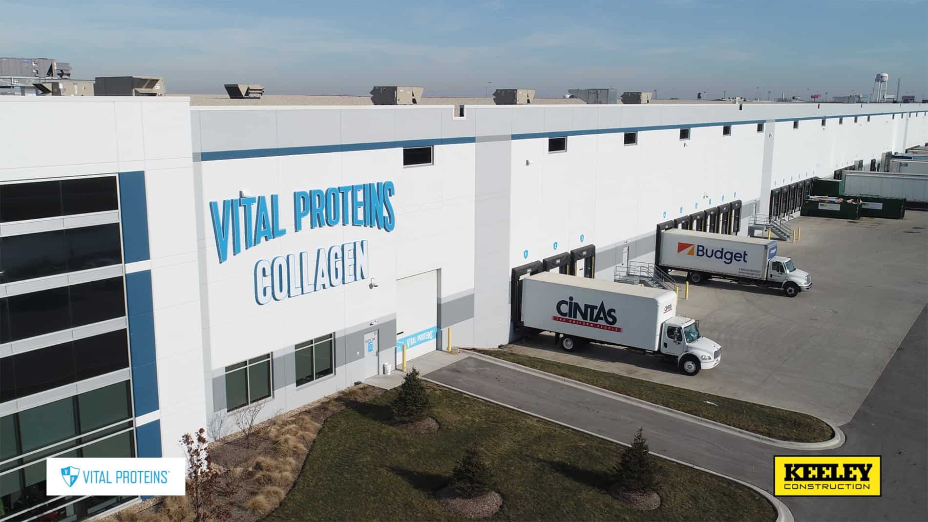 An aerial view of the outside of a long distribution area with docks and semi trucks. A large sign on the side says, "Vital Proteins Collagen."