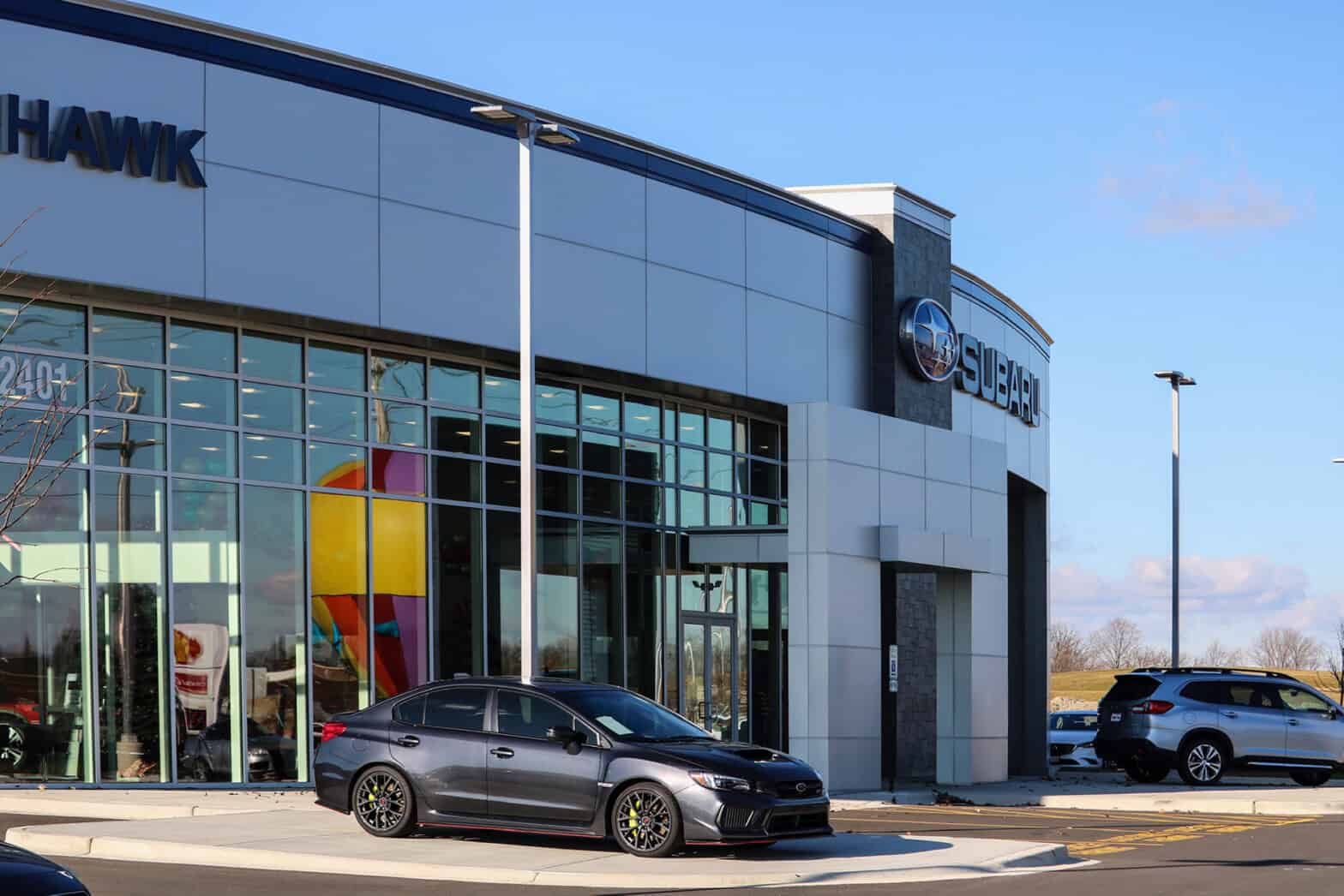 The entrance to the brand-new Hawk Auto is a rounded front with a black car outside the glass wall of the showroom.