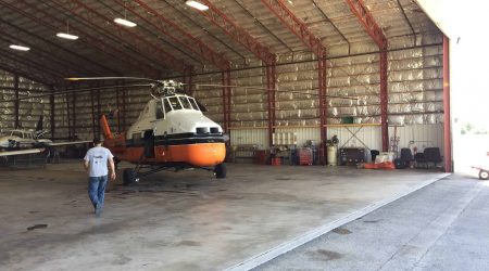 A man in jeans and a t-shirt walks toward a white and orange Midwest Helicopter in a large helicopter hangar built by Keeley Construction, Inc.