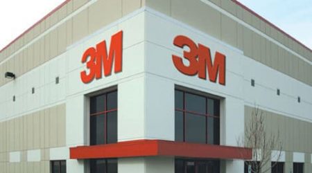 The corner of a 3M building with glass walls and entrances. A big "3M" is on each wall.