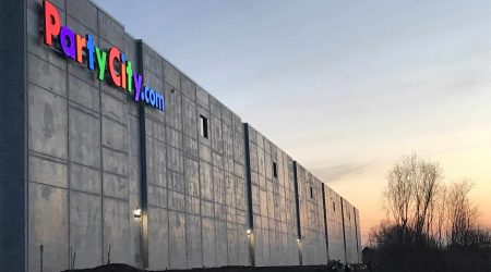 The colorful "Party City" sign illuminates the angled view of the side of the Party City expansion as the sun rises behind the winter trees.
