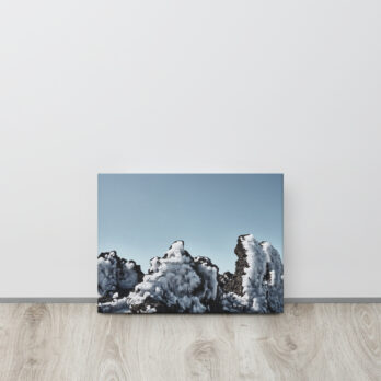 Un cuadro titulado "Lienzo Roque helado", que representa rocas cubiertas de nieve contra un cielo azul claro, se apoya contra una pared blanca sobre un piso de madera clara.