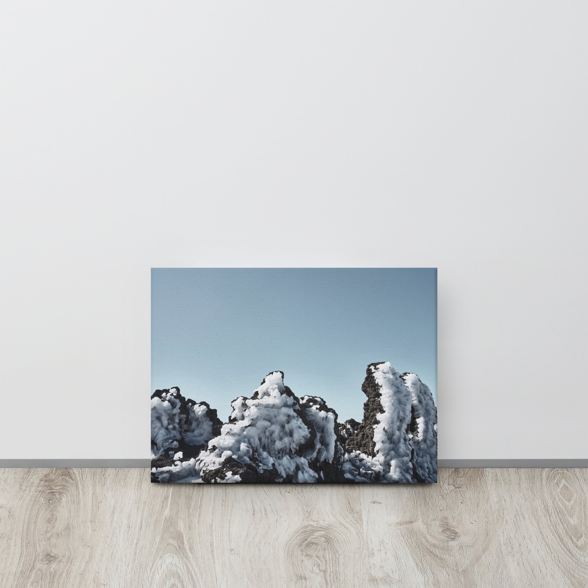 Un cuadro titulado "Lienzo Roque helado", que representa rocas cubiertas de nieve contra un cielo azul claro, se apoya contra una pared blanca sobre un piso de madera clara.