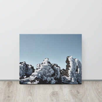 Un lienzo titulado "Lienzo Roque helado", apoyado sobre una pared blanca, muestra un paisaje de formaciones rocosas negras cubiertas de nieve bajo un cielo azul claro. Esta escena tranquila, en contraste con la calidez del suelo de madera, encapsula la belleza distintiva que se encuentra en Paisajes Canarios, similar a Fotografías impresas de Volcanica Productions.