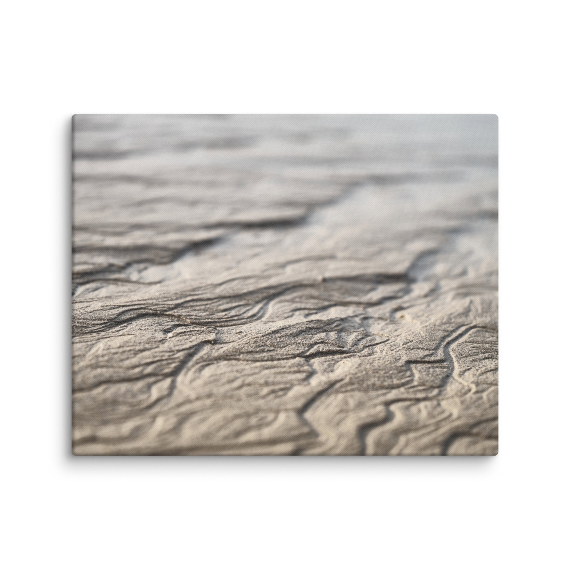 Primer plano de una superficie arenosa con patrones ondulados y texturizados creados por el viento. Esta imagen de "Lienzo surcos arena mojada" muestra líneas y surcos intrincados, que resaltan el diseño natural y las sombras sutiles en la arena. Disponible como Fotografías impresas a través de nuestra Tienda Online.
