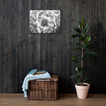 Una planta de caucho en maceta se encuentra sobre un piso de madera junto a una canasta de mimbre llena de libros y una manta doblada. El "Lienzo roca y sal", una exquisita pieza de arte decorativo, cuelga en la pared de madera oscura detrás de ellos.