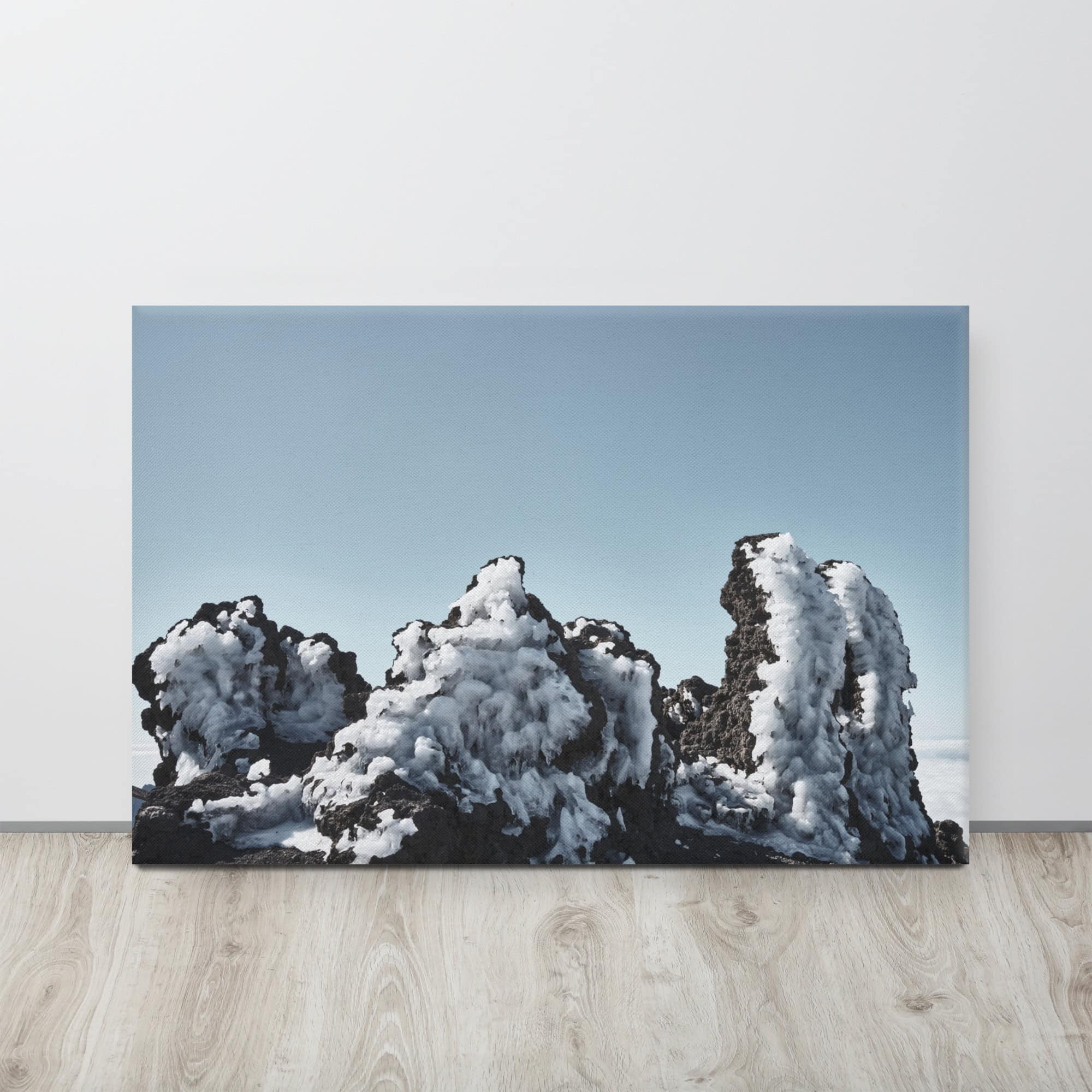 Una fotografía titulada "Lienzo Roque helado", que muestra rocas irregulares cubiertas de nieve bajo un cielo azul claro, sobre un piso de madera. Esta impresionante pieza es parte de la colección de fotografías impresas de Volcanica Productions, inspiradas en la belleza agreste de La Palma.