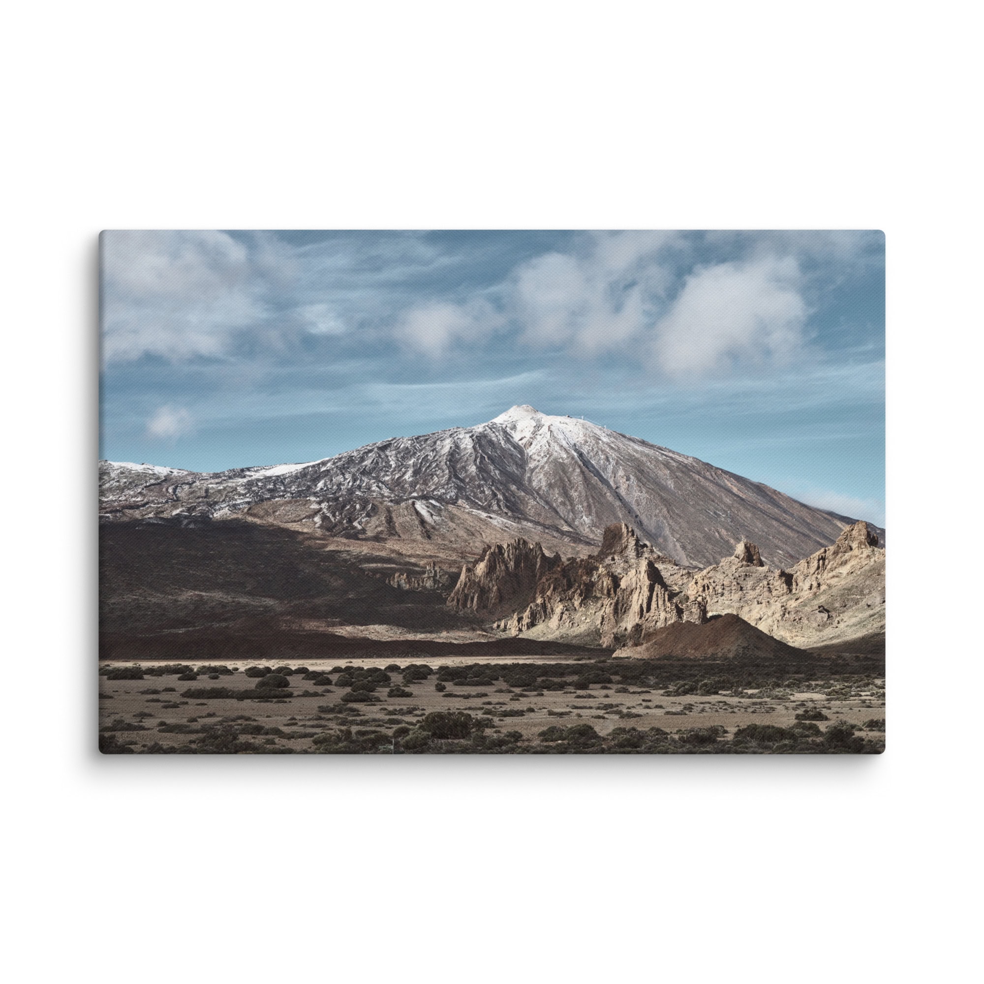 El producto "Lienzo Teide" muestra un vasto paisaje protagonizado por una escarpada cadena montañosa con un pico nevado bajo un cielo parcialmente nublado, complementado por formaciones rocosas marrones y escasa vegetación en primer plano, creando una espectacular escena natural que recuerda a los Paisajes Canarios.