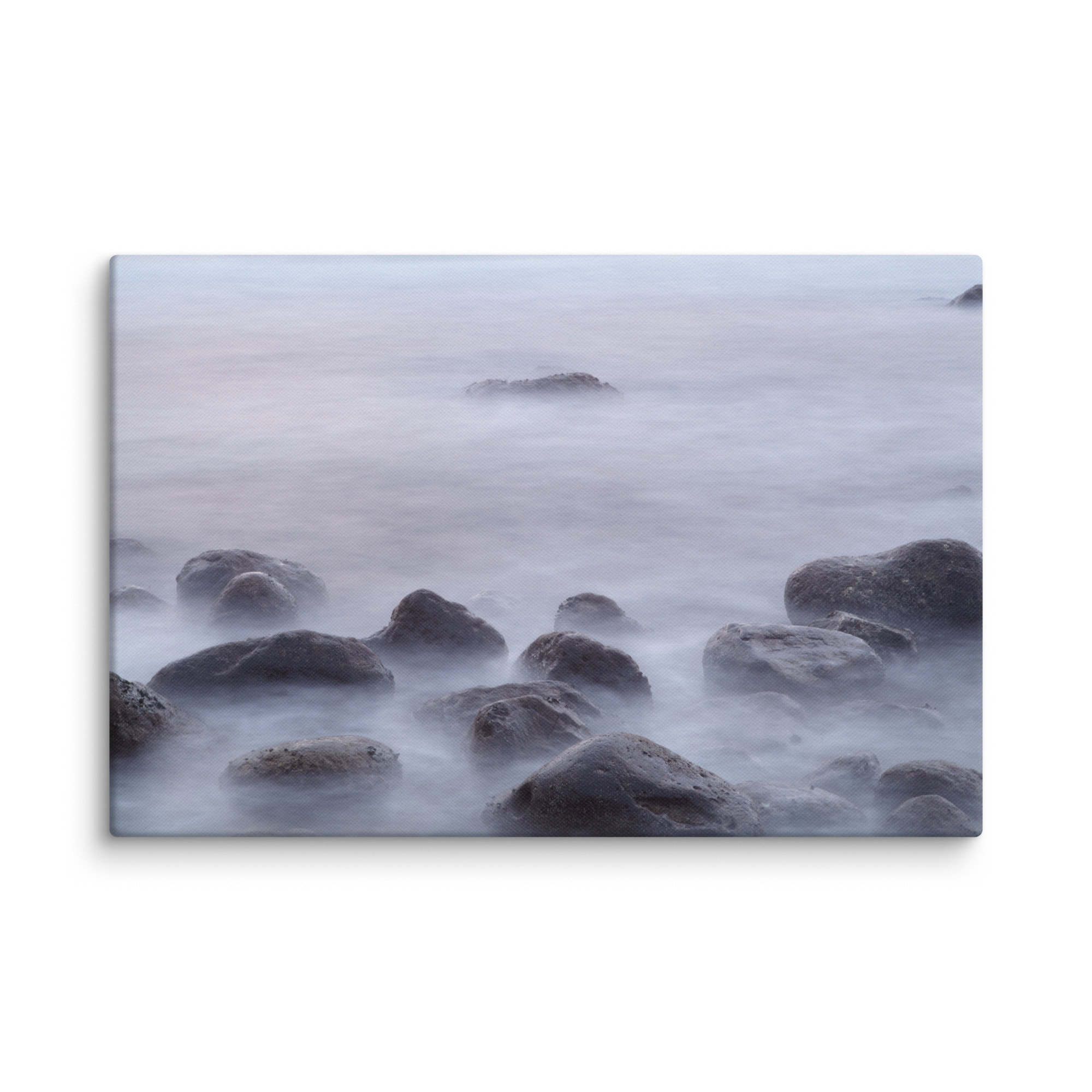 Un paisaje marino sereno con agua suave y brumosa que fluye sobre rocas dispersas crea una atmósfera tranquila bajo un cielo suave y nublado, que recuerda al "Lienzo de Rocas de la playa de El Lloret". Esta escena captura la esencia del Arte Decorativo, perfecta para aquellos que aprecian las buenas fotografías impresas.