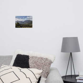Una sala de estar minimalista presenta una lámpara gris sobre una pequeña mesa redonda, un sofá adornado con cojines estampados y el cautivador cartel "Caldera de Taburiente" de Volcanica Productions en la pared blanca. La escena personifica la simplicidad y la decoración moderna.