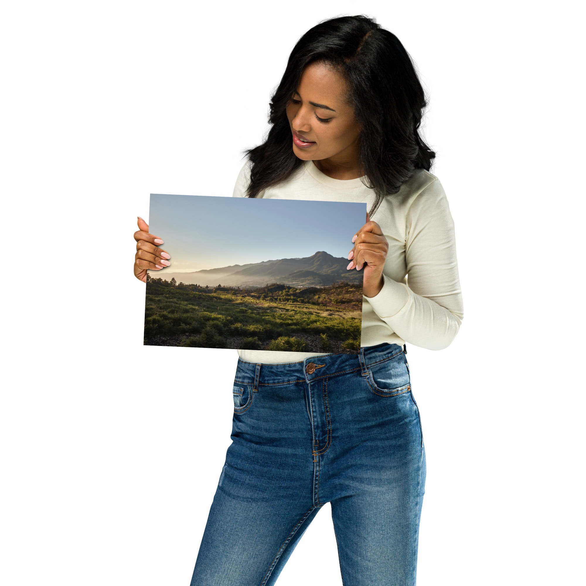 Una mujer con una camisa blanca de manga larga y pantalones vaqueros sostiene el "Póster atardecer desde Cuesta Juliana", que muestra una vista panorámica de la montaña con campos verdes en primer plano bajo el cielo despejado de La Palma.