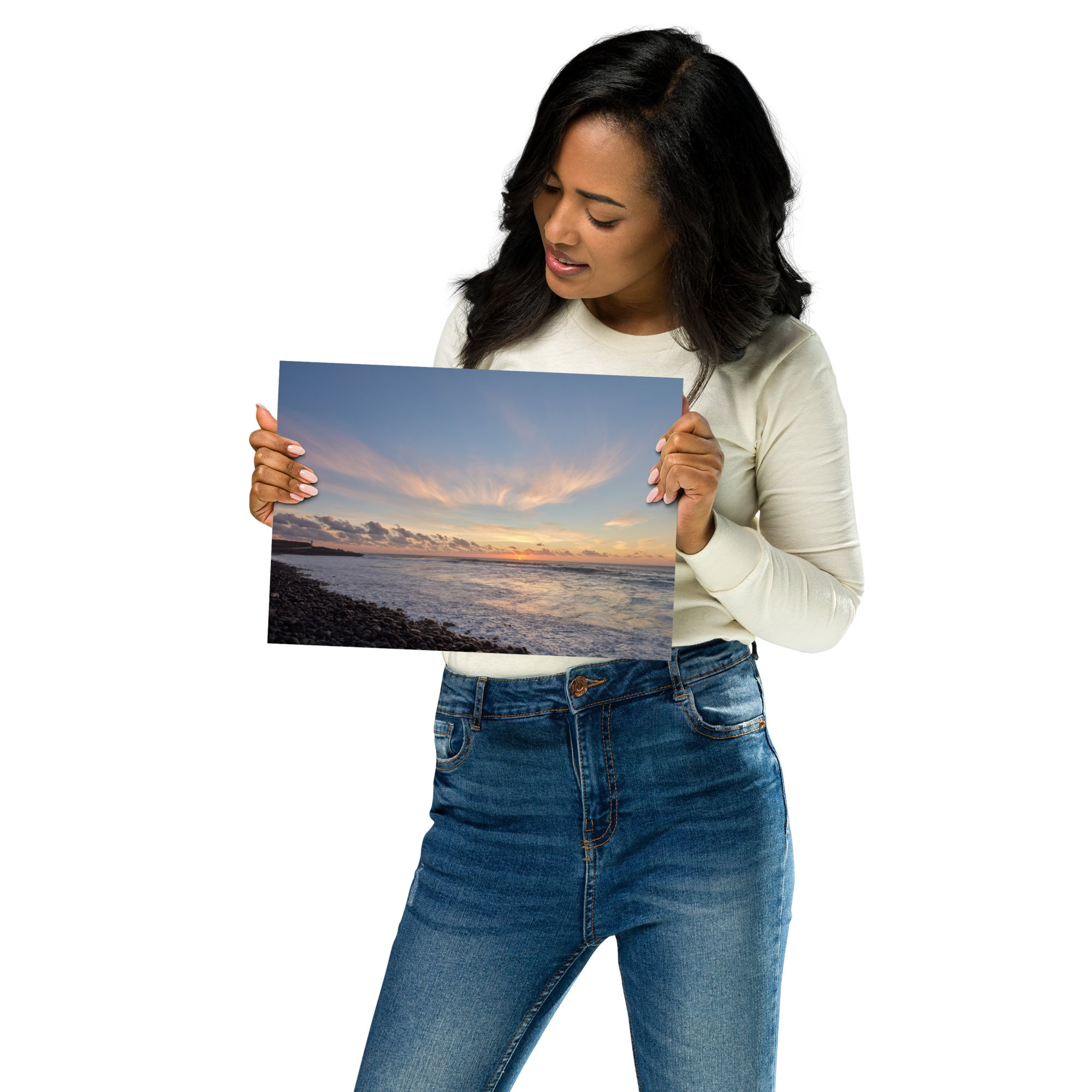 Una mujer con camisa blanca y jeans sostiene una fotografía de un sereno atardecer en la playa, que muestra la tranquilidad de Póster atardecer en Los Guirres. Observa la foto impresa con interés sobre un fondo blanco liso, que recuerda a una visita a la galería seleccionada de una tienda en línea.