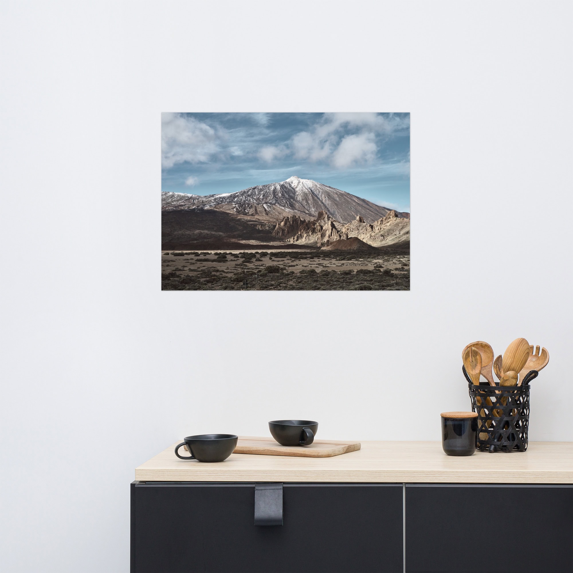 En primer plano se encuentra un mostrador de cocina adornado con tazas negras y un portautensilios, mientras que en la pared blanca cuelga un póster del Teide de Volcanica Productions, que representa una montaña cubierta de nieve bajo un cielo azul, que recuerda las impresionantes vistas de La Palma.