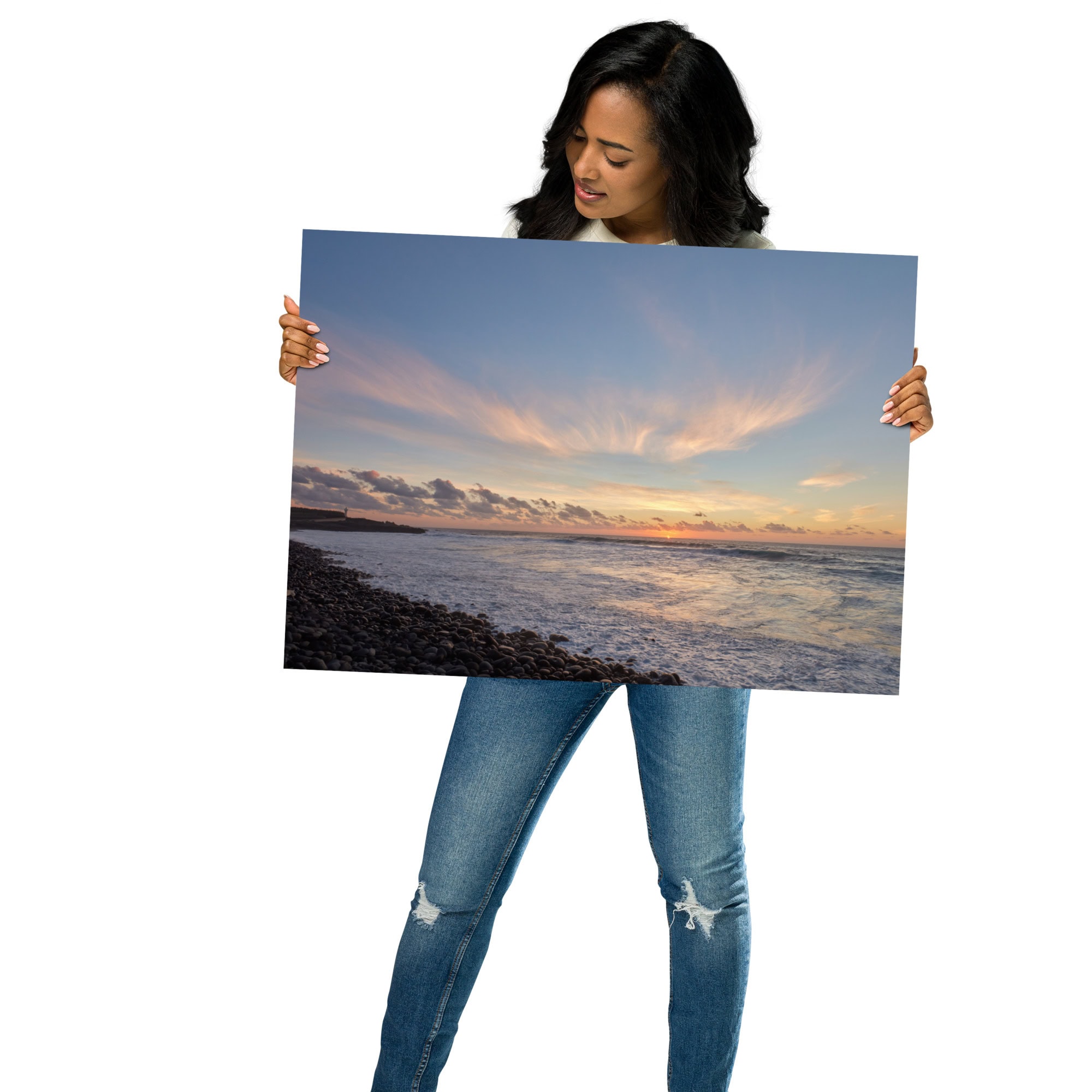 Vestido con jeans azules y una camisa oscura, un individuo sostiene una gran fotografía titulada "Póster atardecer en Los Guirres", que captura un tranquilo atardecer en la playa con nubes y olas, que encarna la esencia de Paisajes Canarios. El fondo blanco liso resalta esta pieza de Arte Decorativo.
