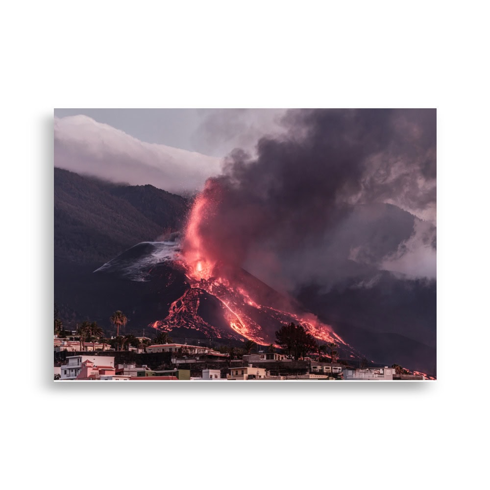 Se captura una exhibición impresionante de la naturaleza cuando el volcán entra en erupción y su lava roja vibrante cae en cascada por las laderas. Espesas columnas de humo oscuro se elevan hacia el cielo, formando un telón de fondo espectacular para las pequeñas estructuras que se encuentran debajo. Este momento, inmortalizado por Volcanica Productions, está encapsulado en su "Póster volcán 2021 La Palma edificios", que muestra arte decorativo en movimiento.