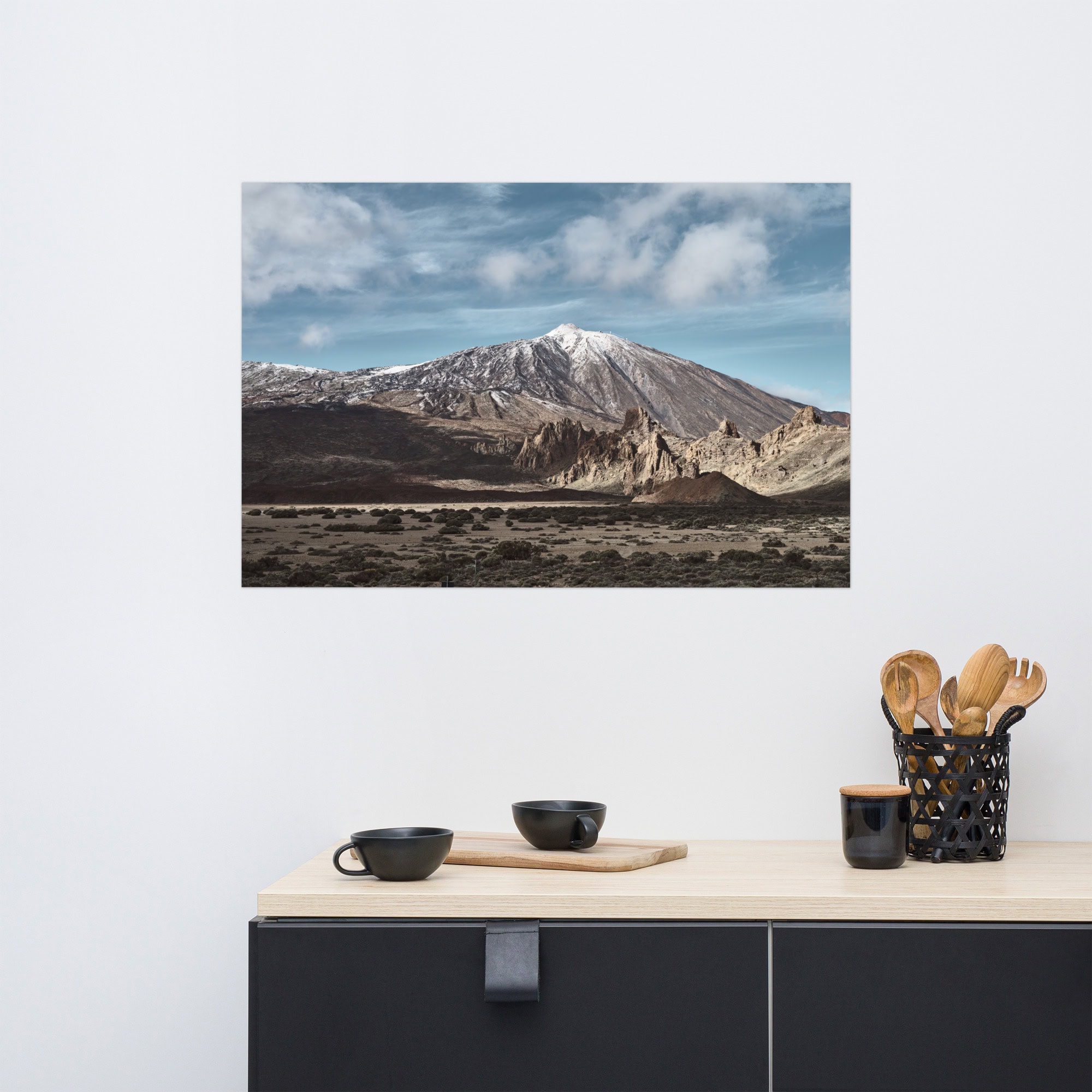 El póster "Teide" muestra una impresionante fotografía de un paisaje de una montaña nevada bajo un cielo azul nublado, ideal para colocar sobre un estante de cocina moderno. Esta pieza de Volcanica Productions combina a la perfección con elementos negros y de madera, con utensilios en un soporte y dos cuencos negros, ideales para agregar elegancia a su tienda online.