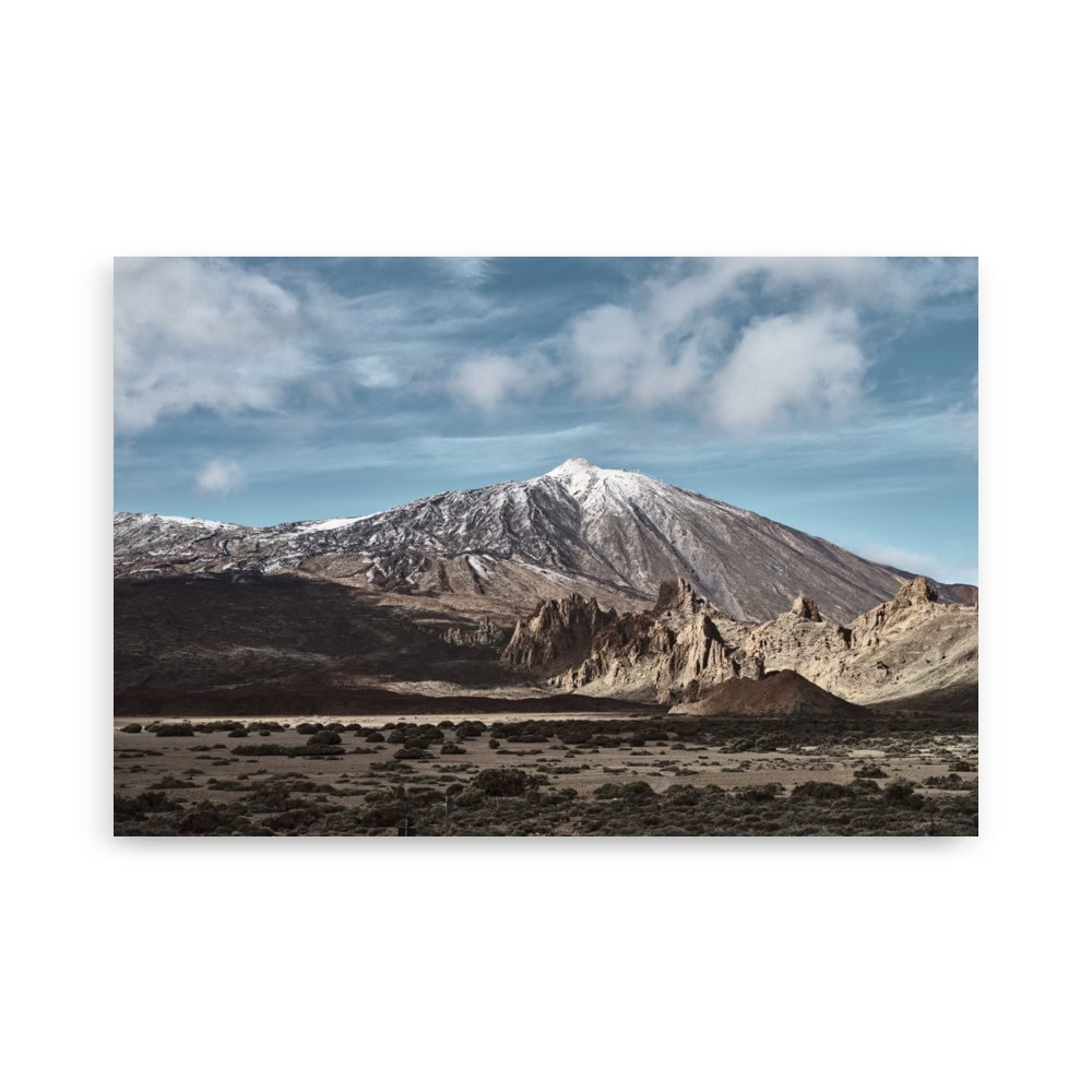 Descubra los impresionantes Paisajes Canarios con nuestro Póster Teide, disponible en nuestra Tienda Online como impresionantes fotografías impresas para adornar su espacio. Este póster presenta una montaña cubierta de nieve bajo un cielo azul con nubes dispersas, complementado por formaciones rocosas escarpadas y un primer plano cubierto de arena y matorrales.