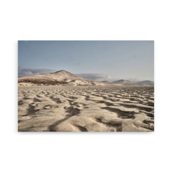 El póster Sotavento muestra un extenso paisaje desértico con ondulantes dunas de arena bajo un cielo azul claro, acentuado por las montañas en el fondo. Esta serena vista, capturada por Volcanica Productions, presenta sombras en las dunas que crean un patrón texturizado en toda la escena.