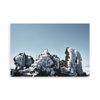 Las rocas volcánicas cubiertas de nieve, que recuerdan al póster Roque helado de Volcanica Productions, se destacan contra un cielo azul claro. Las formaciones escarpadas están cubiertas de nieve, lo que crea una escena natural sorprendente que se asemeja al arte decorativo de la galería de la naturaleza.