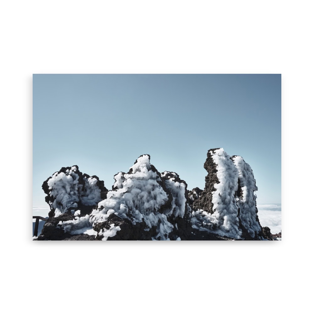 Las rocas volcánicas cubiertas de nieve, que recuerdan al póster Roque helado de Volcanica Productions, se destacan contra un cielo azul claro. Las formaciones escarpadas están cubiertas de nieve, lo que crea una escena natural sorprendente que se asemeja al arte decorativo de la galería de la naturaleza.