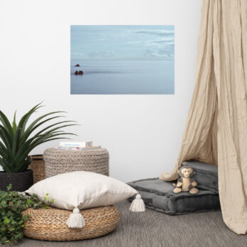 Un acogedor espacio de estar presenta una fotografía en la pared de un paisaje marino en calma, que recuerda al póster Mar en Calma en Los Cancajos. La habitación incluye una planta, una pila de libros, cestas tejidas, asientos acolchados en el suelo y un mono de juguete, lo que crea una atmósfera serena y acogedora enriquecida por esta pieza de Arte Decorativo.