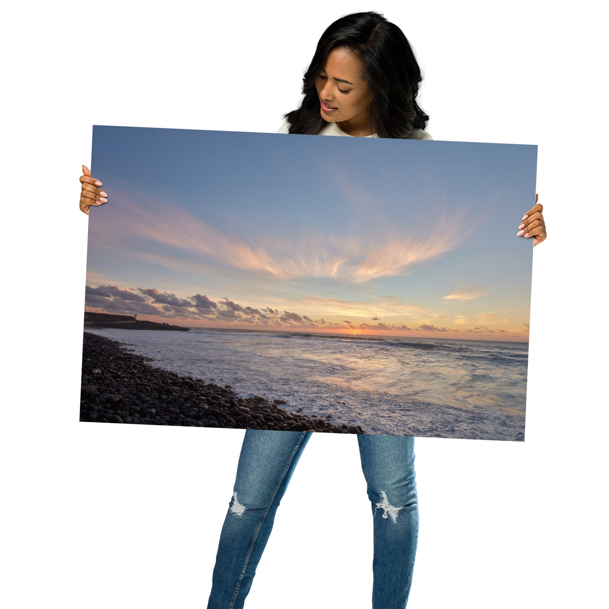Una persona con ropa informal sostiene una gran e impresionante fotografía impresa titulada "Póster atardecer en Los Guirres" de Volcanica Productions, que captura una pintoresca puesta de sol en la playa. La imagen muestra una costa de guijarros, olas del océano y nubes iluminadas por el sol poniente: una pieza perfecta para quienes buscan fotografías impresas exquisitas.
