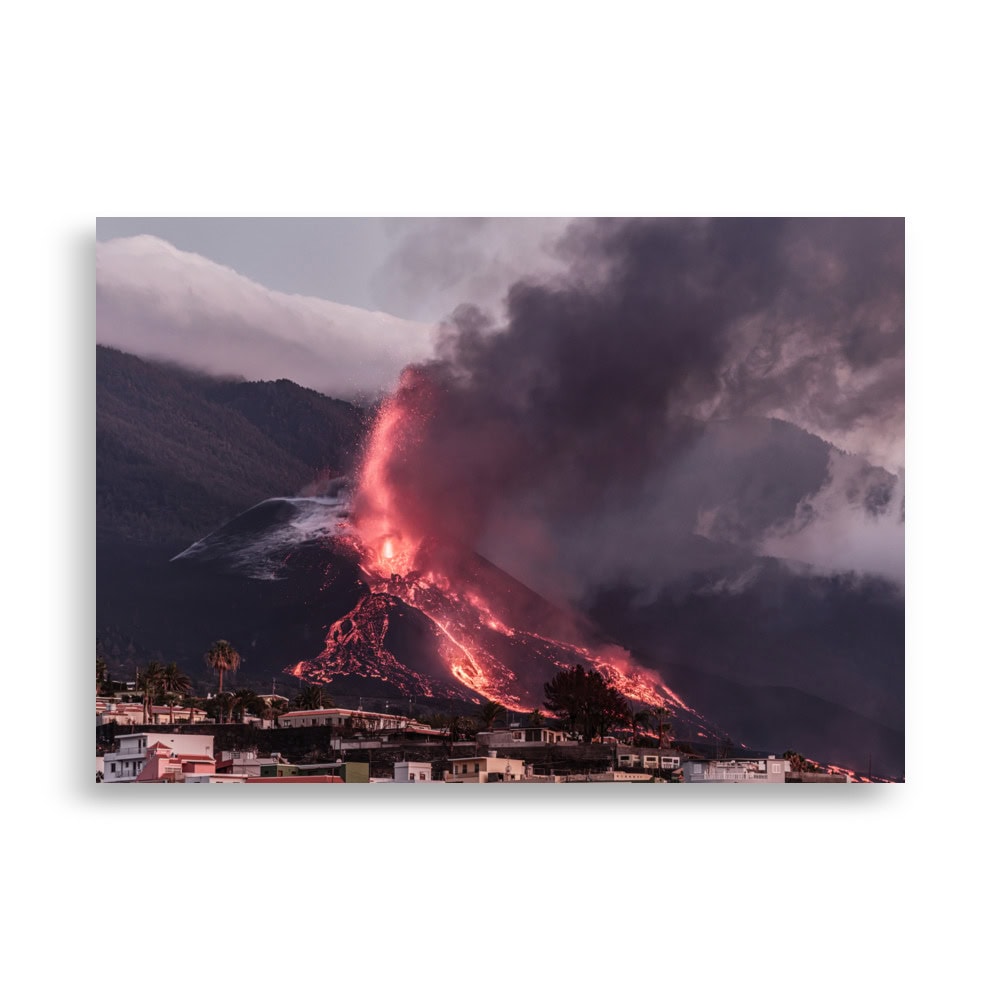 Una escena cautivadora de la erupción de un volcán en La Palma presenta ríos de lava resplandecientes y humo oscuro que se eleva hacia el cielo. La silueta de un pueblo en primer plano agrega profundidad a esta imagen impactante, ideal para quienes buscan un "Póster volcán 2021 La Palma edificios" espectacular o arte decorativo único para su espacio.