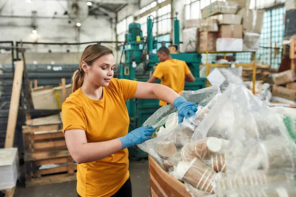 Young woman puts disposables into bags at a recycling facility