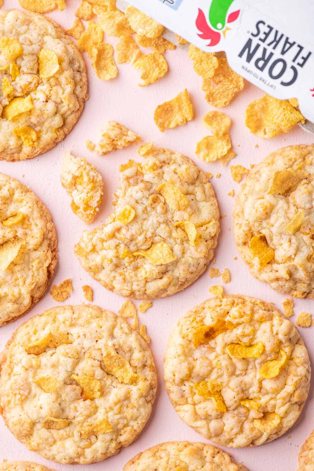 Close-up of crispy cornflake cookies with scattered cereal flakes on a pink background