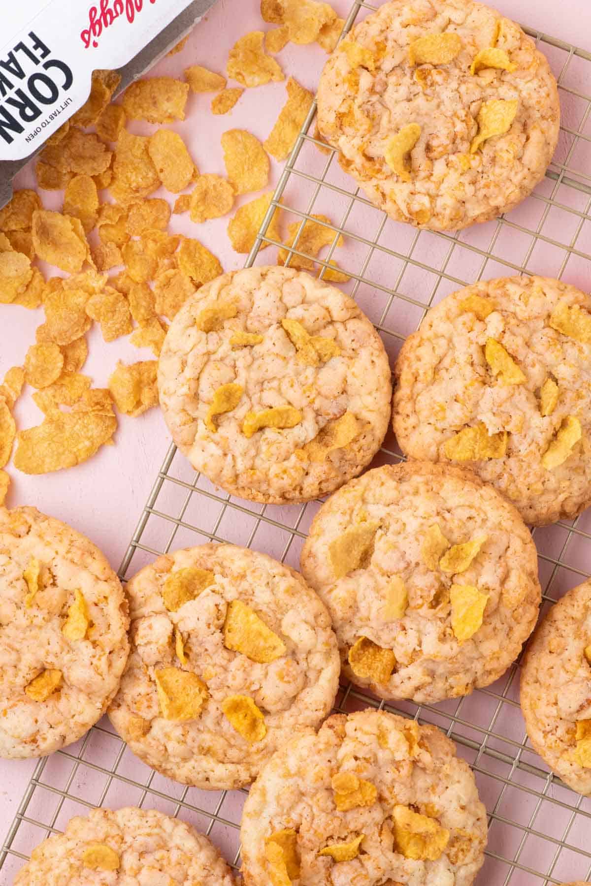 Freshly baked cornflake cookies cooling on a wire rack with cereal flakes scattered around.