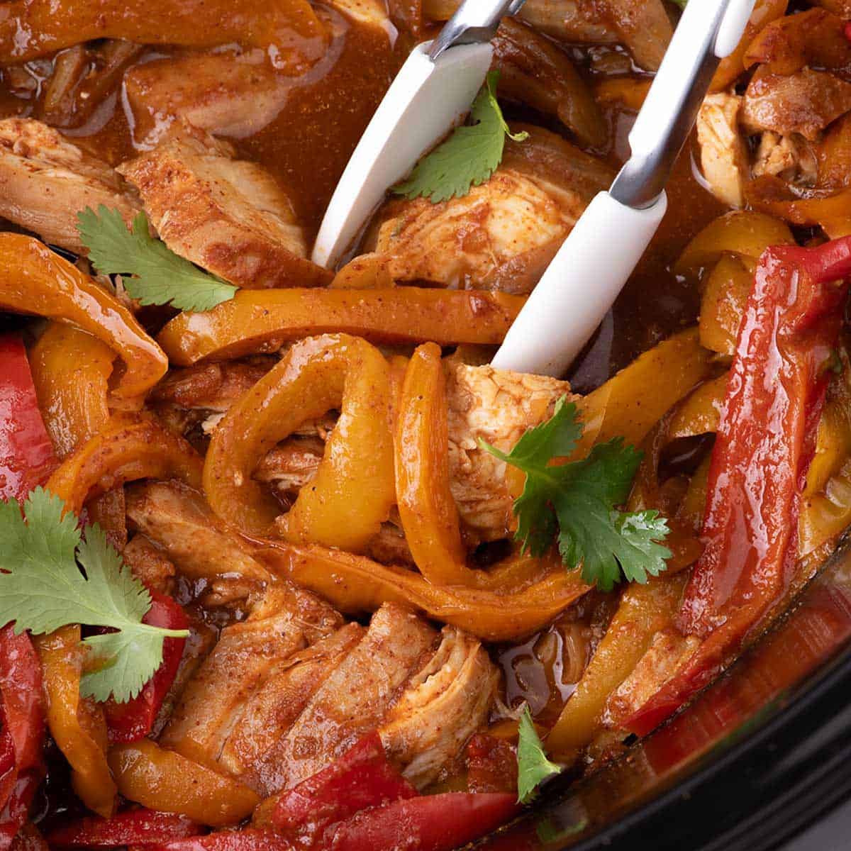 Close-up of juicy slow cooker chicken fajitas with tender sliced chicken, red and yellow bell peppers, sweet onion, and fresh cilantro in a rich homemade sauce.