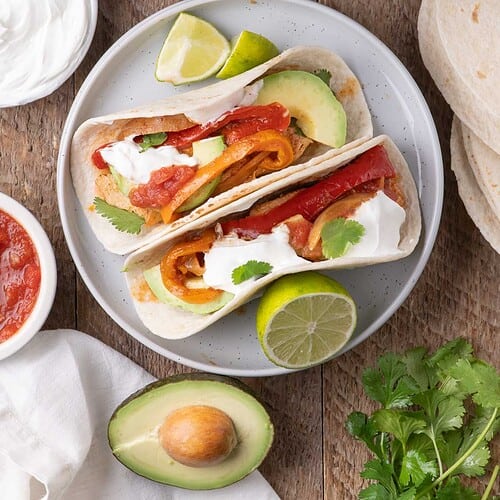 Family-style spread of slow cooker chicken fajitas with tortillas, toppings, and garnishes on a rustic table