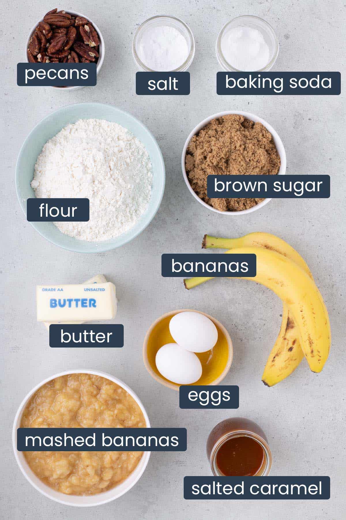 Overhead view of ingredients for salted caramel banana bread bars including bananas, pecans, flour, brown sugar, eggs, butter, and salted caramel.